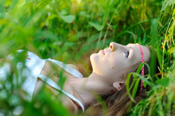 Giovane bella ragazza slava con i capelli lunghi e abbigliamento etnico slavo si trova nell'erba in una foresta estiva — Foto Stock