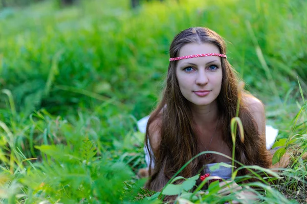 Menina eslava bonita nova com cabelos longos e trajes étnicos eslavos encontra-se na grama em uma floresta de verão — Fotografia de Stock