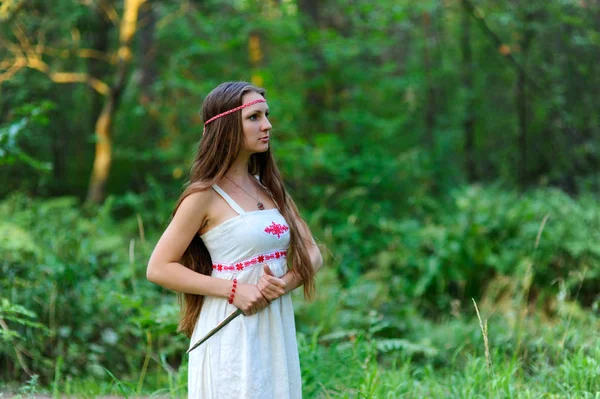 Молодая красивая славянская девушка с длинными волосами и славянской этнической одеждой стоит в летнем лесу с ритуальным кинжалом в руках — стоковое фото