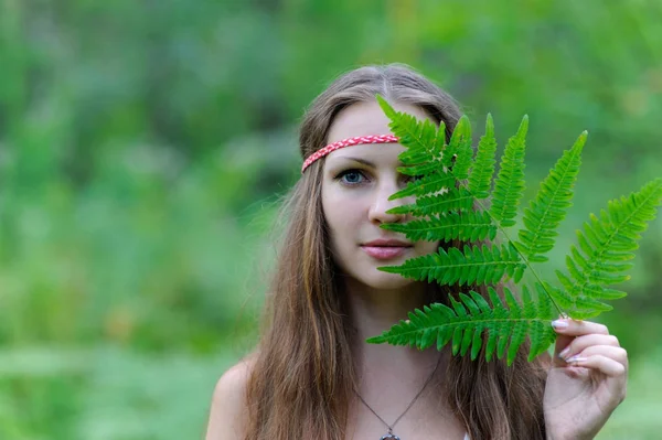 Eine junge schöne slawische Mädchen mit langen Haaren und slawischen ethnischen Kleid bedeckte ihr Gesicht mit einem Farnblatt — Stockfoto