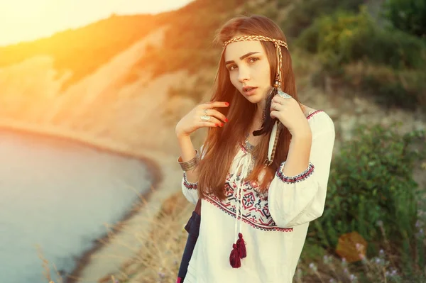 Beautiful brunette girl in Bocho chic style stands on the background of the sea in the rays of a bright sun. Vintage color tone — Stock Photo, Image