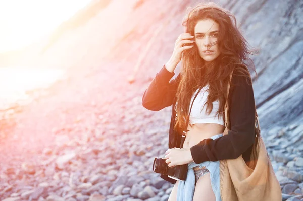 Menina no estilo de boho com uma câmera no mar nos raios de um sol brilhante — Fotografia de Stock