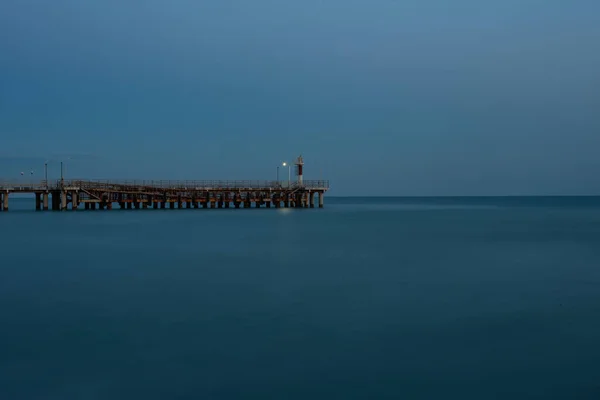 Little sea lighthouse on the pier. Calm sea. Minimalism. Dusk. Calm and silence