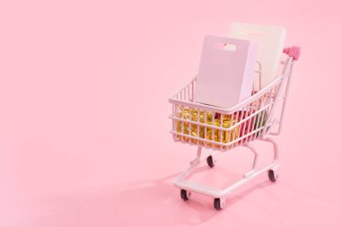 Geleneksel alışveriş sezonu konsepti - soluk pembe arka planda izole edilmiş kağıt çanta dolu mini pembe alışveriş arabası, boş fotokopi alanı, kapat