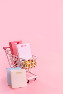 Geleneksel alışveriş sezonu konsepti - soluk pembe arka planda izole edilmiş kağıt çanta dolu mini pembe alışveriş arabası, boş fotokopi alanı, kapat