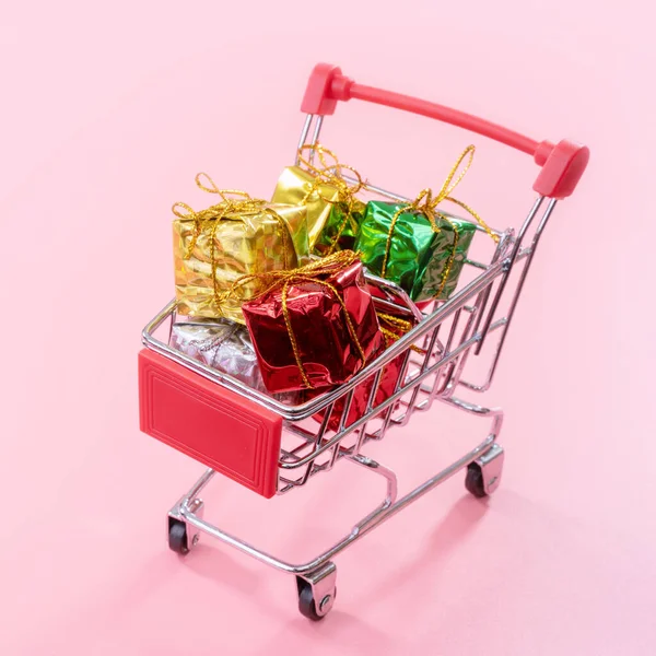 Jaarlijkse verkoop, kerst shopping seizoen concept-mini rode winkel kar trolley vol met geschenk doos geïsoleerd op bleke roze achtergrond, kopieer ruimte, close-up — Stockfoto