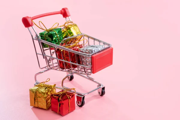 Jaarlijkse verkoop, kerst shopping seizoen concept-mini rode winkel kar trolley vol met geschenk doos geïsoleerd op bleke roze achtergrond, kopieer ruimte, close-up — Stockfoto