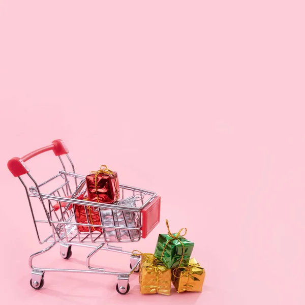 Jaarlijkse verkoop, kerst shopping seizoen concept-mini rode winkel kar trolley vol met geschenk doos geïsoleerd op bleke roze achtergrond, kopieer ruimte, close-up — Stockfoto
