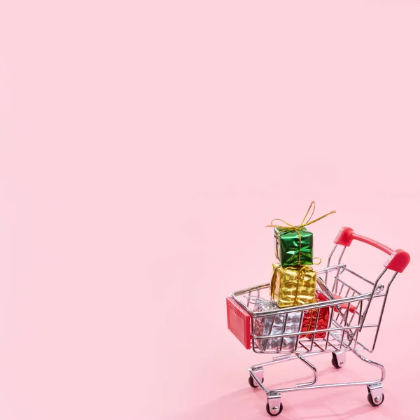 Jaarlijkse verkoop, kerst shopping seizoen concept-mini rode winkel kar trolley vol met geschenk doos geïsoleerd op bleke roze achtergrond, kopieer ruimte, close-up — Stockfoto