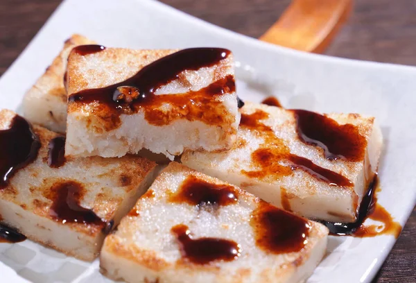 Gieten van zwarte sojasaus op kant-en-klare heerlijke rapkoek, Chinese traditionele lokale schotel radijs taart in restaurant, close-up, kopieer ruimte. — Stockfoto