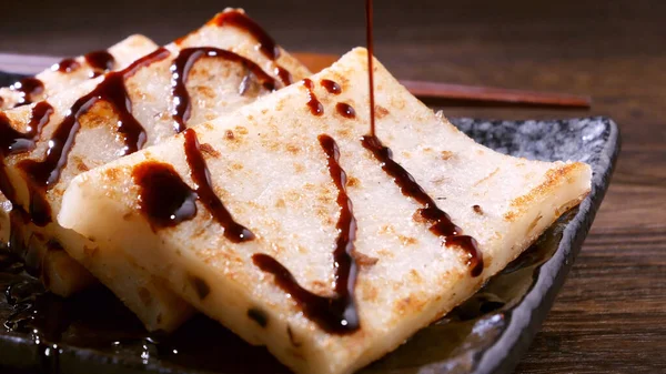 Verter salsa de soja negra en el delicioso pastel de nabo listo para comer, plato tradicional chino pastel de rábano en el restaurante, primer plano, espacio para copiar . — Foto de Stock