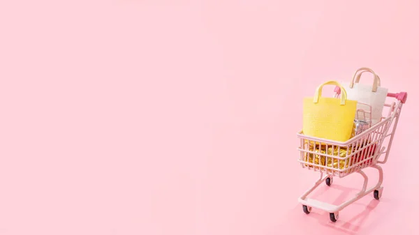 Vente annuelle concept de saison d'achat - mini chariot de chariot de magasin rose plein de sac en papier cadeau isolé sur fond rose pâle, espace de copie vierge, gros plan — Photo