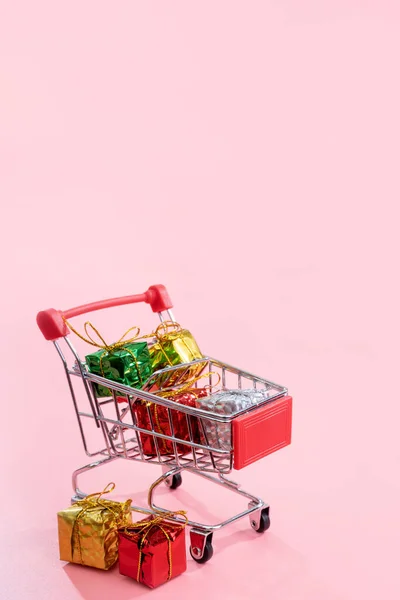 Jaarlijkse verkoop, kerst shopping seizoen concept-mini rode winkel kar trolley vol met geschenk doos geïsoleerd op bleke roze achtergrond, kopieer ruimte, close-up — Stockfoto