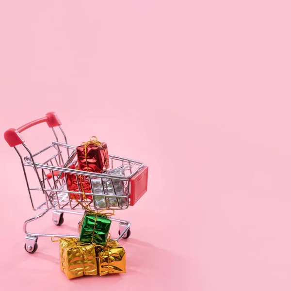 Jaarlijkse verkoop, kerst shopping seizoen concept-mini rode winkel kar trolley vol met geschenk doos geïsoleerd op bleke roze achtergrond, kopieer ruimte, close-up — Stockfoto