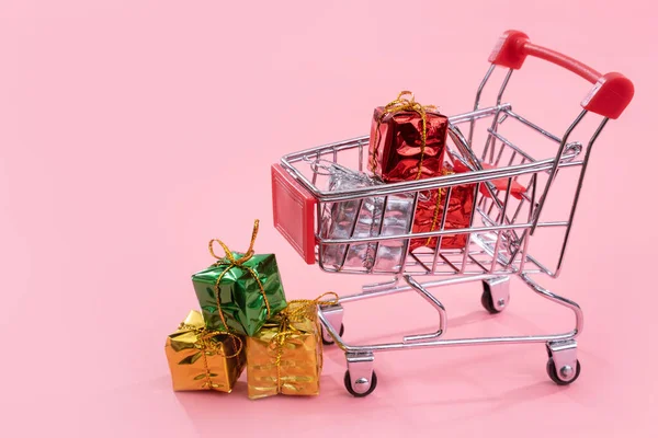 Jaarlijkse verkoop, kerst shopping seizoen concept-mini rode winkel kar trolley vol met geschenk doos geïsoleerd op bleke roze achtergrond, kopieer ruimte, close-up — Stockfoto