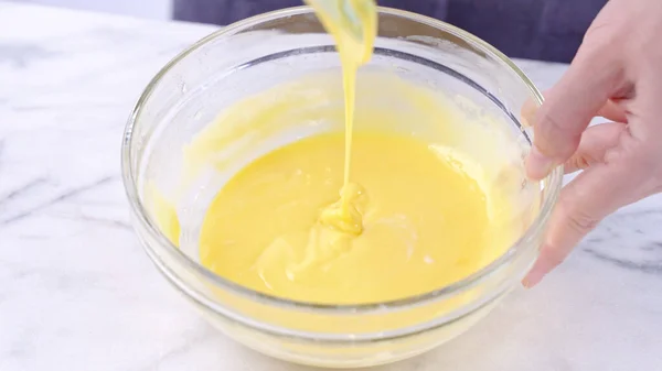 Mixing egg yolk into cake batter with green rubber spatula mixer tool stirring until smooth and blend well in a glass bowl, close up, lifestyle — Stock Photo, Image