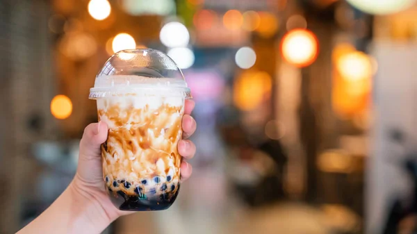 Mujer joven está sosteniendo, beber azúcar moreno con sabor a tapioca perla té de leche de burbuja con paja de vidrio en el mercado nocturno de Taiwán, de cerca, bokeh — Foto de Stock