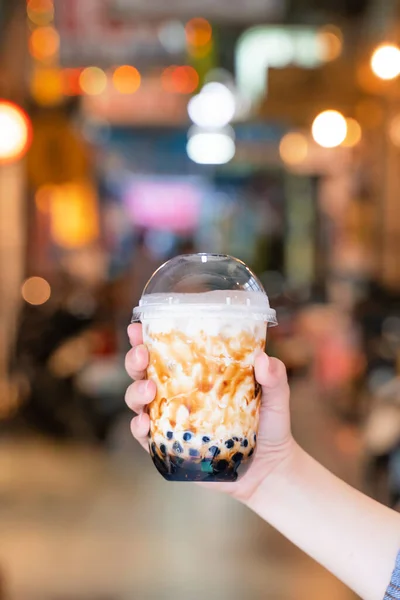 Mujer joven está sosteniendo, beber azúcar moreno con sabor a tapioca perla té de leche de burbuja con paja de vidrio en el mercado nocturno de Taiwán, de cerca, bokeh — Foto de Stock