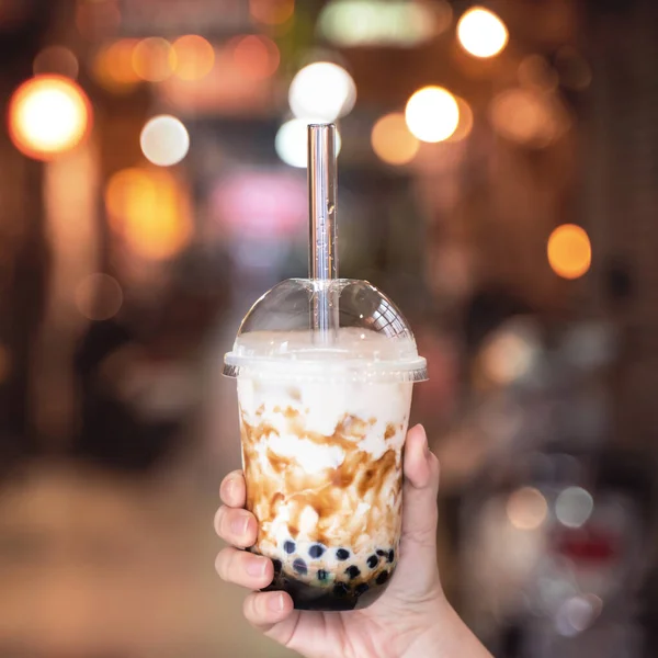 Mujer joven está sosteniendo, beber azúcar moreno con sabor a tapioca perla té de leche de burbuja con paja de vidrio en el mercado nocturno de Taiwán, de cerca, bokeh — Foto de Stock