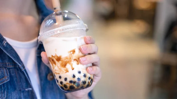 Mujer joven está sosteniendo, beber azúcar moreno con sabor a tapioca perla té de leche de burbuja con paja de vidrio en el mercado nocturno de Taiwán, de cerca, bokeh — Foto de Stock