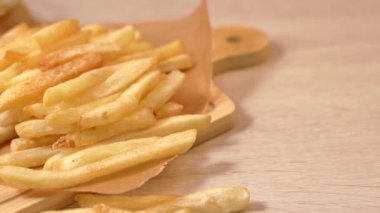 Yağda kızartılmış altın gibi nefis patates kızartmalarını parşömen kağıdında görmek ve yemek, kapanış, yaşam tarzı için kesme tahtası sunmak..