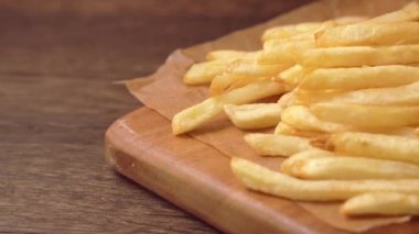 Yağda kızartılmış altın gibi nefis patates kızartmalarını parşömen kağıdında görmek ve yemek, kapanış, yaşam tarzı için kesme tahtası sunmak..