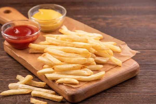 Batatas fritas douradas deliciosas em papel de assar kraft e bandeja de servir para comer com ketchup e mostarda amarela, close-up, estilo de vida . — Fotografia de Stock