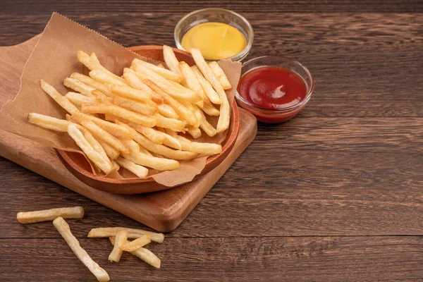 Golden yummy deep French fries on kraft baking sheet paper and serving tray to eat with ketchup and yellow mustard, close up, lifestyle.