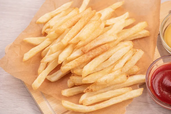 Goldene leckere Pommes frites auf Kraftblattpapier und Servierblech zum Essen mit Ketchup und gelbem Senf, Nahaufnahme, Lifestyle. — Stockfoto