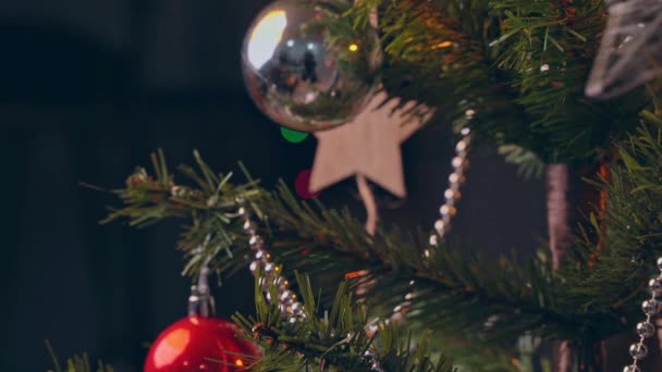 一个女人把圣诞装饰品挂在圣诞树枝叶上 近距离拍摄 在漆黑的黑色背景下闪烁着闪光的线路灯 — 图库视频影像