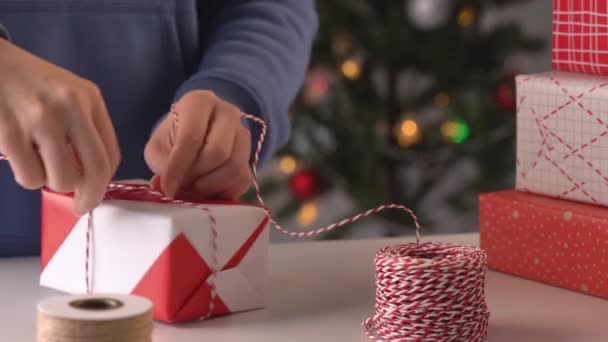 一位身穿蓝色衣服的年轻女子正在用漂亮 红白相间的包装纸包装着送给孩子们的圣诞礼物 包装纸上闪烁着亮晶晶的光芒和生活方式 — 图库视频影像