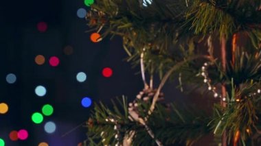 Bir kız Noel ağacına Noel süsü asıyor, yakın plan, koyu siyah arka planda kıvılcım saçan lamba ışığı ile..