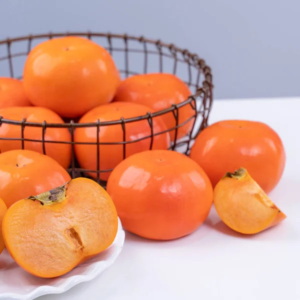 Fresh beautiful sliced sweet persimmon kaki isolated on white kitchen table with gray blue background, Chinese lunar new year design concept, close up. — Stock Photo, Image
