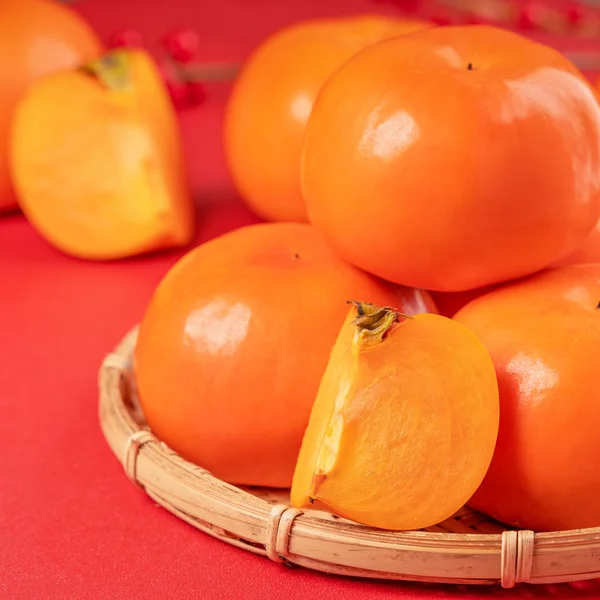 Fraîche belle tranchée kaki persimmon doux isolé sur fond de table rouge et tamis en bambou, chinois lunaire nouvelle année concept de conception, gros plan . — Photo