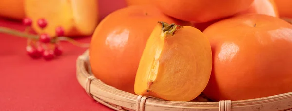 Fresh beautiful sliced sweet persimmon kaki isolated on red table background and bamboo κόσκινο, Κινέζικο σεληνιακό σχέδιο. — Φωτογραφία Αρχείου