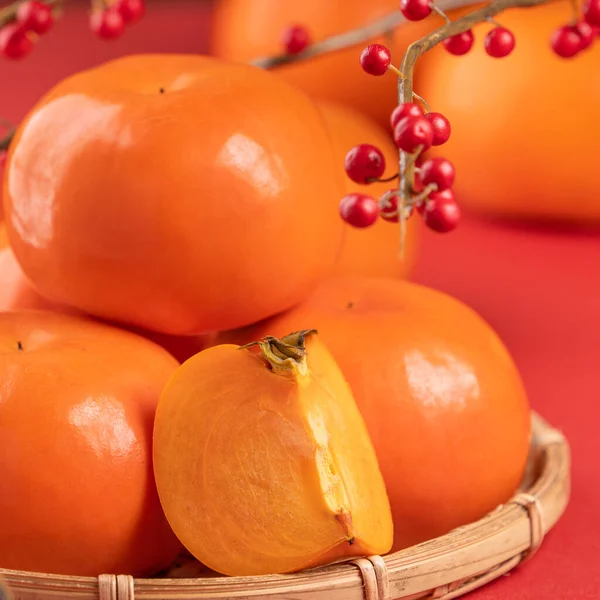 Fresh beautiful sliced sweet persimmon kaki isolated on red table background and bamboo sieve, Chinese lunar new year design concept, close up. — Stock Photo, Image