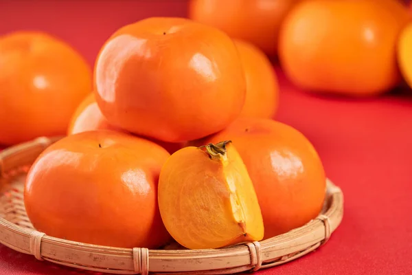 Frische schöne in Scheiben geschnittene süße Persimmon Kaki isoliert auf rotem Tischhintergrund und Bambussieb, chinesisches Mondneujahr Designkonzept, Nahaufnahme. — Stockfoto