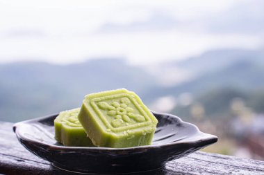 Tayvan 'da bir çay evinin ahşap parmaklıklarında siyah çay tabağıyla nefis yeşil fasulyeli kek. Arka planda güzel bir manzara var..