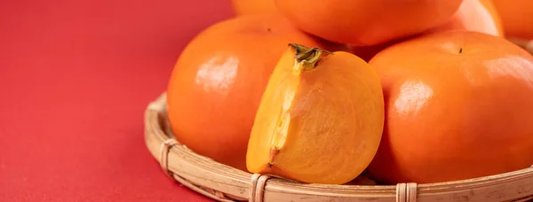 Fresh beautiful sliced sweet persimmon kaki isolated on red table background and bamboo κόσκινο, Κινέζικο σεληνιακό σχέδιο. — Φωτογραφία Αρχείου