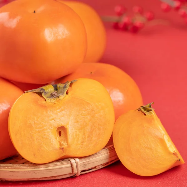 Fresh beautiful sliced sweet persimmon kaki isolated on red table background and bamboo sieve, Chinese lunar new year design concept, close up. — Stock Photo, Image