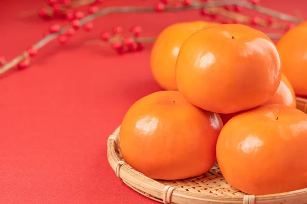 Fresh beautiful sliced sweet persimmon kaki isolated on red table background and bamboo sieve, Chinese lunar new year design concept, close up. — Stock Photo, Image