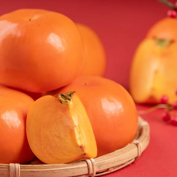 Frische schöne in Scheiben geschnittene süße Persimmon Kaki isoliert auf rotem Tischhintergrund und Bambussieb, chinesisches Mondneujahr Designkonzept, Nahaufnahme. — Stockfoto