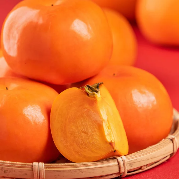 Frische schöne in Scheiben geschnittene süße Persimmon Kaki isoliert auf rotem Tischhintergrund und Bambussieb, chinesisches Mondneujahr Designkonzept, Nahaufnahme. — Stockfoto