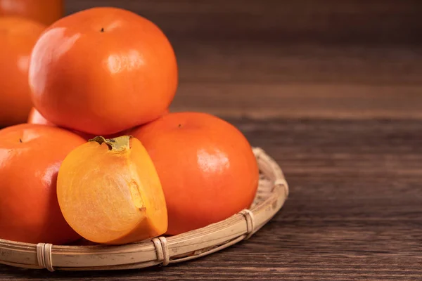 Fresh, beautiful orange color persimmon kaki on bamboo sieve over dark wooden table. Seasonal, traditional fruit of Chinese lunar new year, close up. — Stock Photo, Image