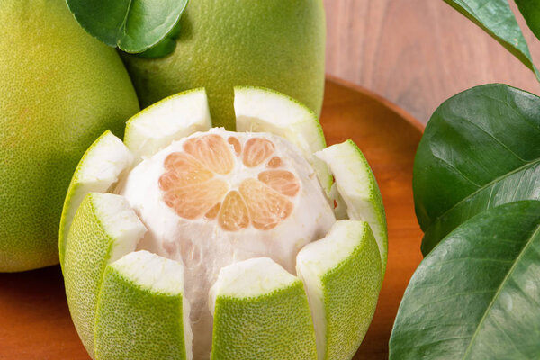 Fresh peeled pomelo, grapefruit, shaddock with green leaves on dark wooden plank table. Seasonal fruit near mid-autumn festival, close up, copy space
