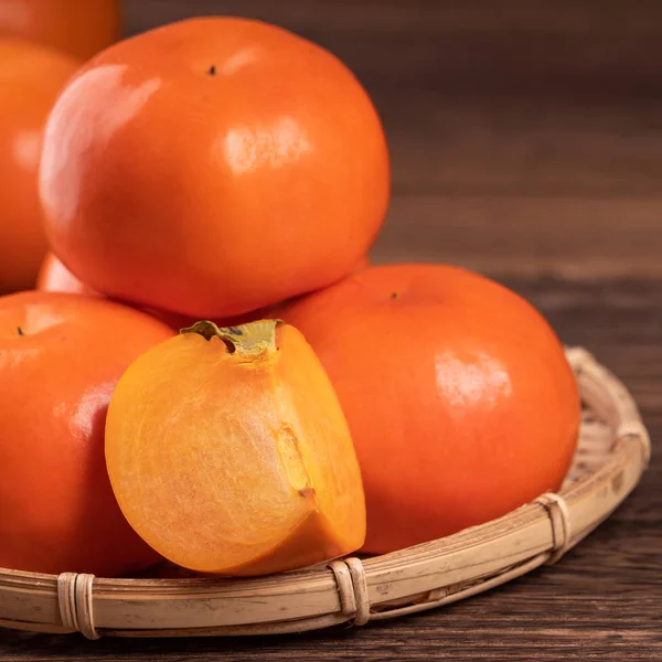 Frische, schöne orange Farbe persimmon Kaki auf Bambussieb über dunklem Holztisch. saisonale, traditionelle Früchte des chinesischen Mondneujahres aus nächster Nähe. — Stockfoto