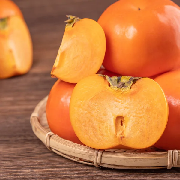 Frische, schöne orange Farbe persimmon Kaki auf Bambussieb über dunklem Holztisch. saisonale, traditionelle Früchte des chinesischen Mondneujahres aus nächster Nähe. — Stockfoto