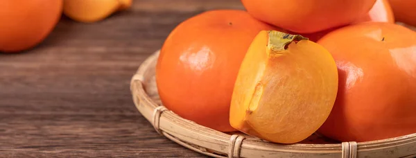 Fresh, beautiful orange color persimmon kaki on bamboo sieve over dark wooden table. Seasonal, traditional fruit of Chinese lunar new year, close up. — Stock Photo, Image