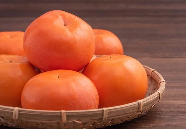 濃い木製のテーブルの上に竹のふるいに新鮮な、美しいオレンジ色の柿の木。中国の旧正月の季節、伝統的な果物、クローズアップ. — ストック写真