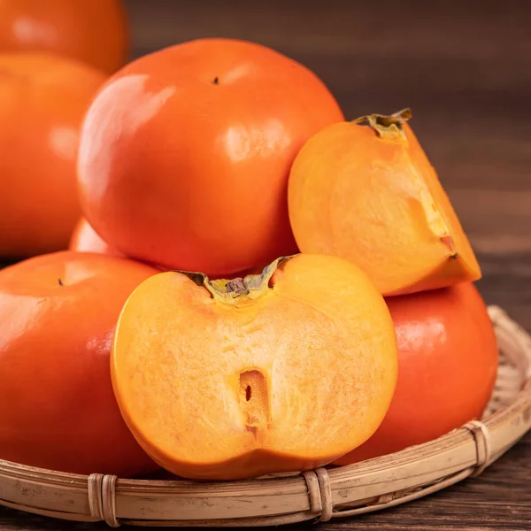 Fresco, hermoso color naranja caqui kaki en el tamiz de bambú sobre la mesa de madera oscura. Fruta estacional, tradicional del año nuevo lunar chino, primer plano . — Foto de Stock